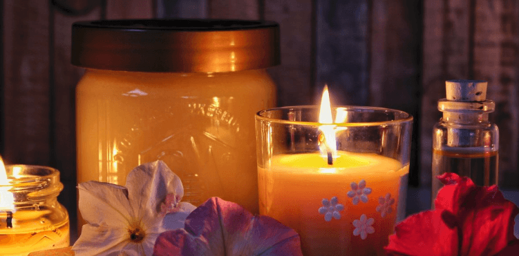 lilin aromaterapi yang menyala, dengan kelopak bunga dan botol parfum di sekitarnya
